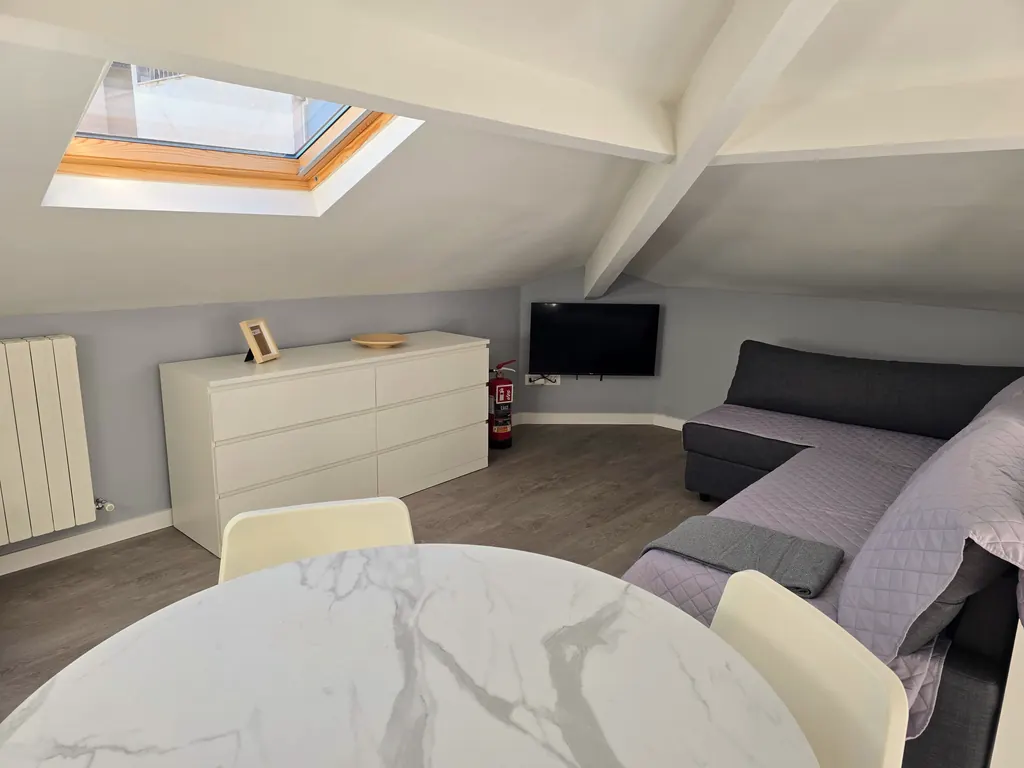 Tavolo rotondo effetto marmo con divano letto e televisore sotto il lucernario
